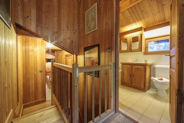 Interior em madeira com escada que leva a um banheiro com vaso sanitário e armários de madeira.