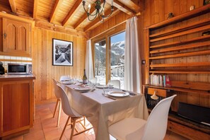 A wooden interior with a dining table set for four, a kitchen area, and a bookshelf.