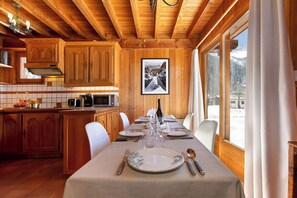 A wooden interior with a dining table set for four, kitchen appliances, and a framed picture on the wall.