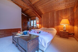 A wooden room with a bed, bedside table, lamp, and a small table with bread and a candle.