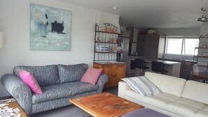 En stue med en stribet sofa, en hvid sofa, et træ sofabord og en reol.