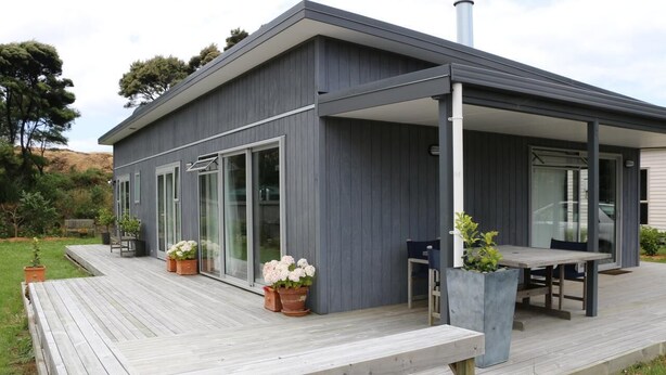 Et moderne hus med en overdækket terrasse, store skydedøre og plantekasser.