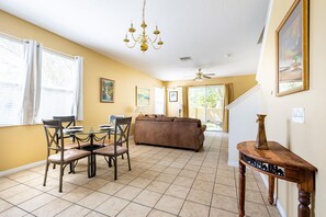 A dining area with a glass table and chairs, a brown sofa, a chandelier, and a ceiling fan.