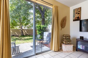 A room with a sliding glass door leading to a garden, a flat-screen TV, and a small bookshelf.