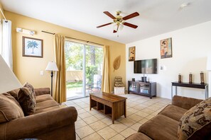 A living room with a ceiling fan, a TV, and a sliding glass door leading to an outdoor area.