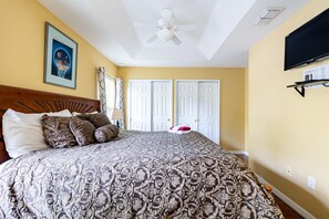 A bedroom with a bed, a ceiling fan, a TV mounted on the wall, and a framed picture on the wall.