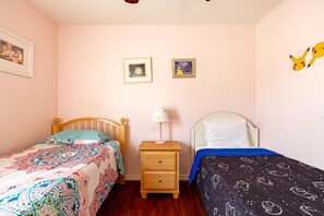 A bedroom with two single beds, a nightstand with a lamp, and two framed pictures on the wall.
