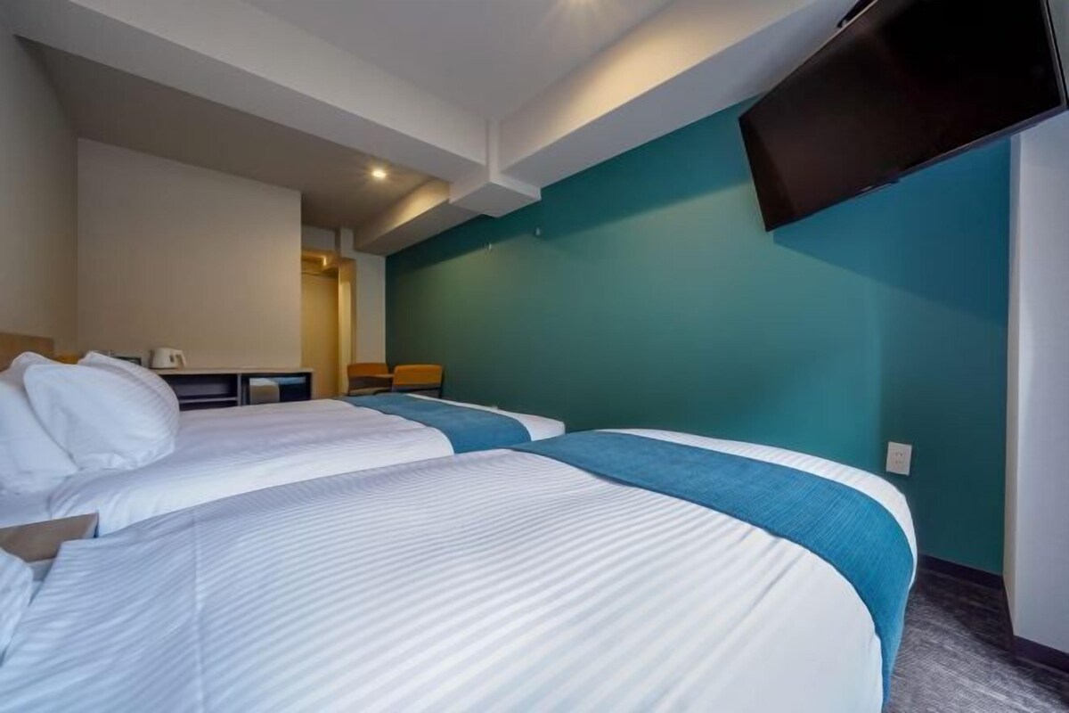 A hotel room with two beds, a flat-screen TV mounted on the wall, and a small seating area with a table and chairs.