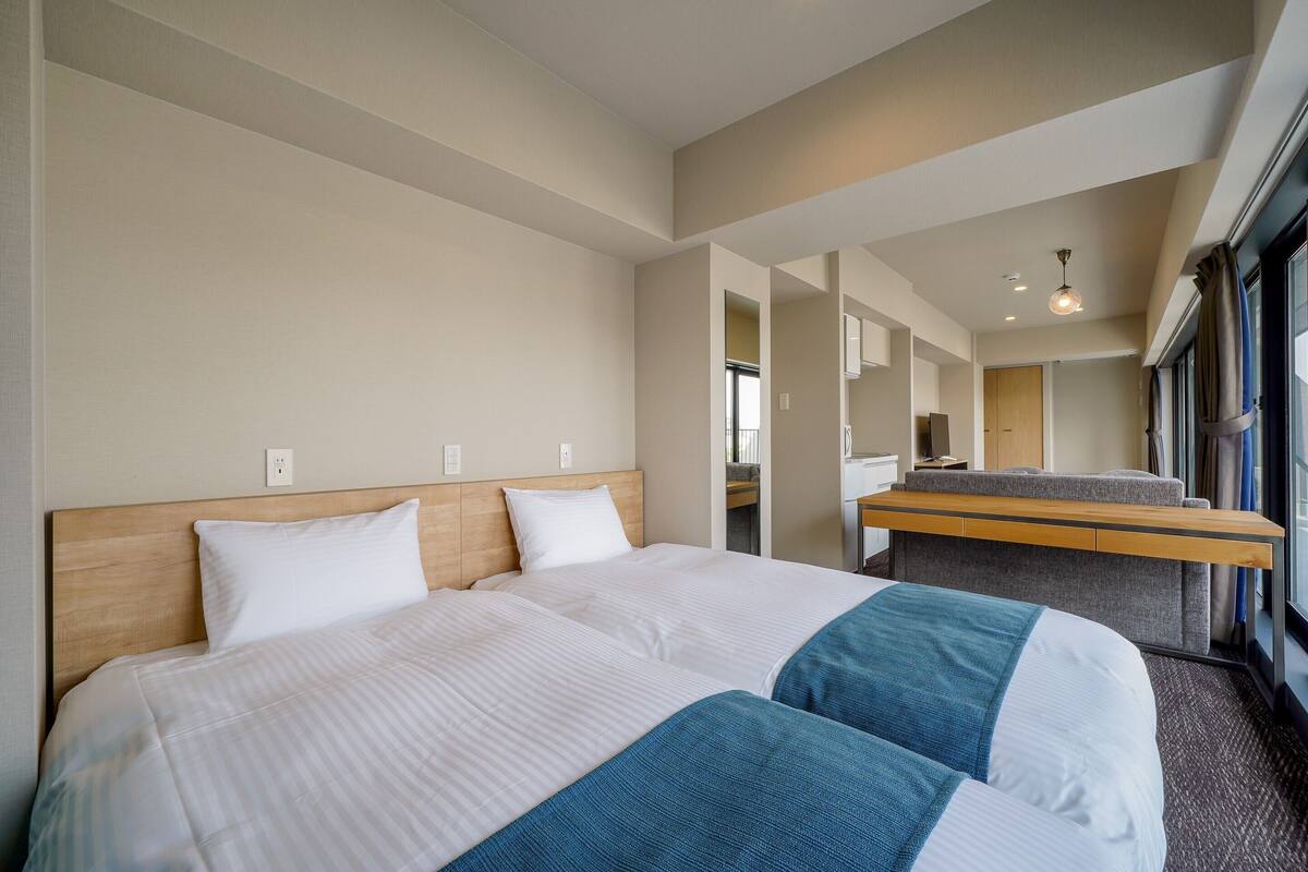A hotel room with two beds, a desk, and a view of the city.