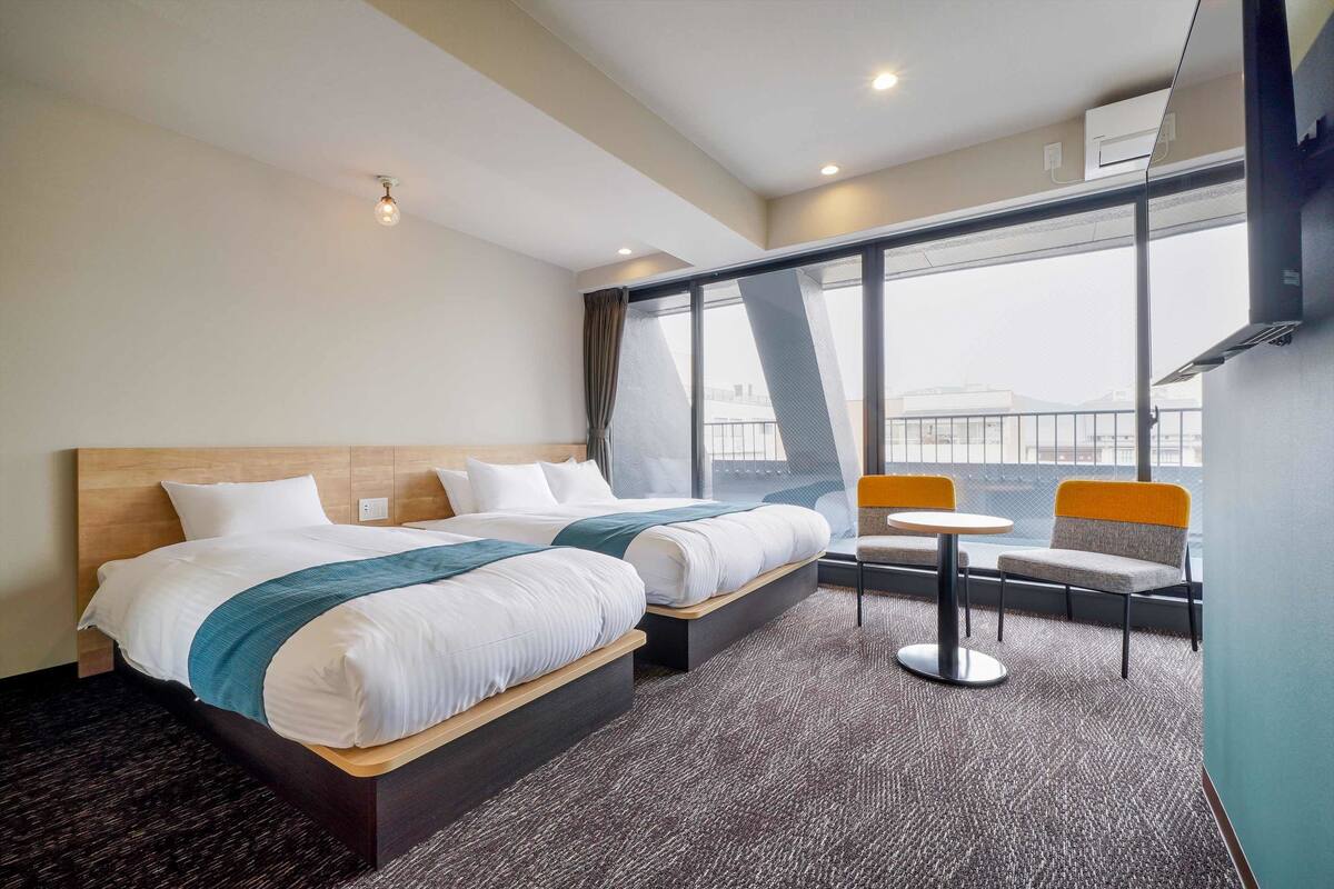 A hotel room with two beds, a small table, and chairs, a large window with a view, and a modern design.