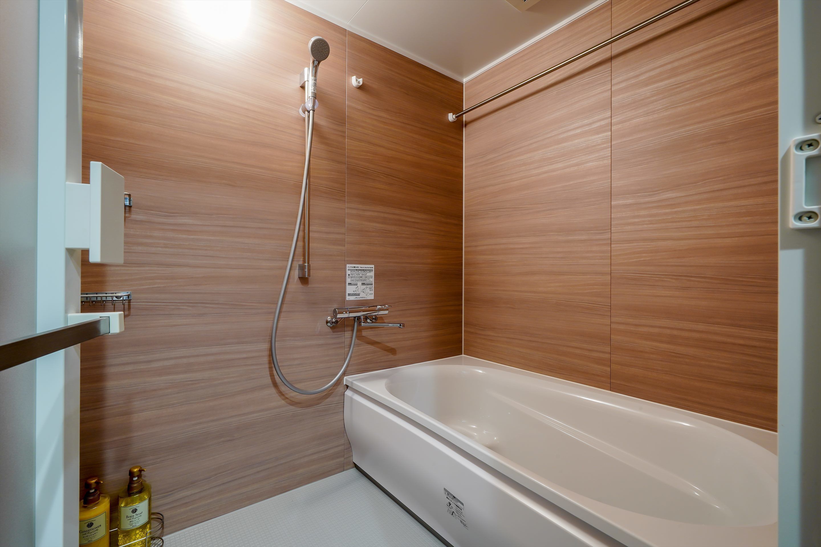 A modern bathroom with a wooden wall, a white bathtub, and a shower with a handheld showerhead.
