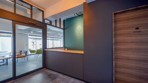 A modern office space with glass partitions, a reception area with a green wall, and a wooden door labeled "storage". - RESI STAY HEART (Kyoto)