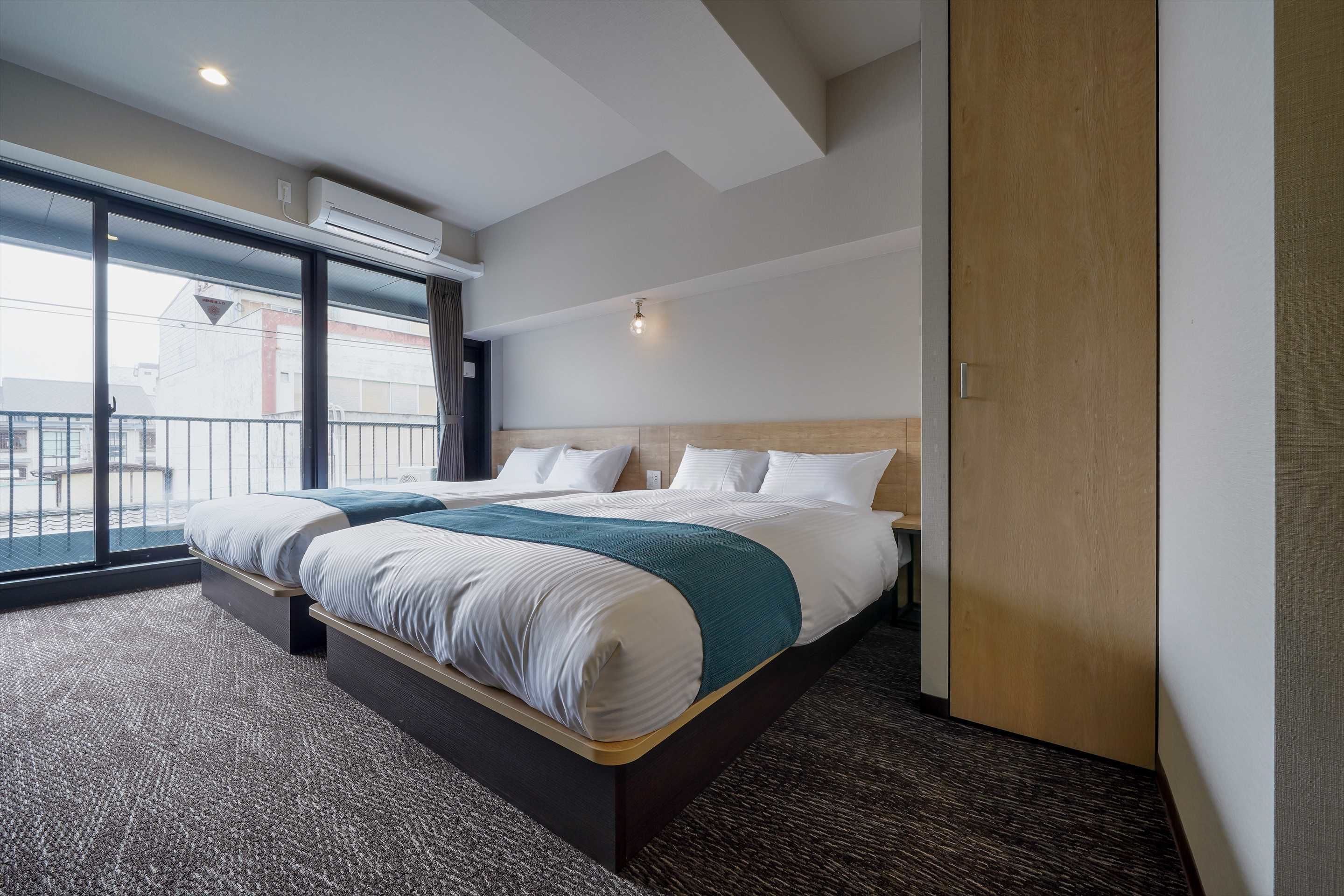 A hotel room with a large bed, a view through a sliding door, and an air conditioning unit on the wall.