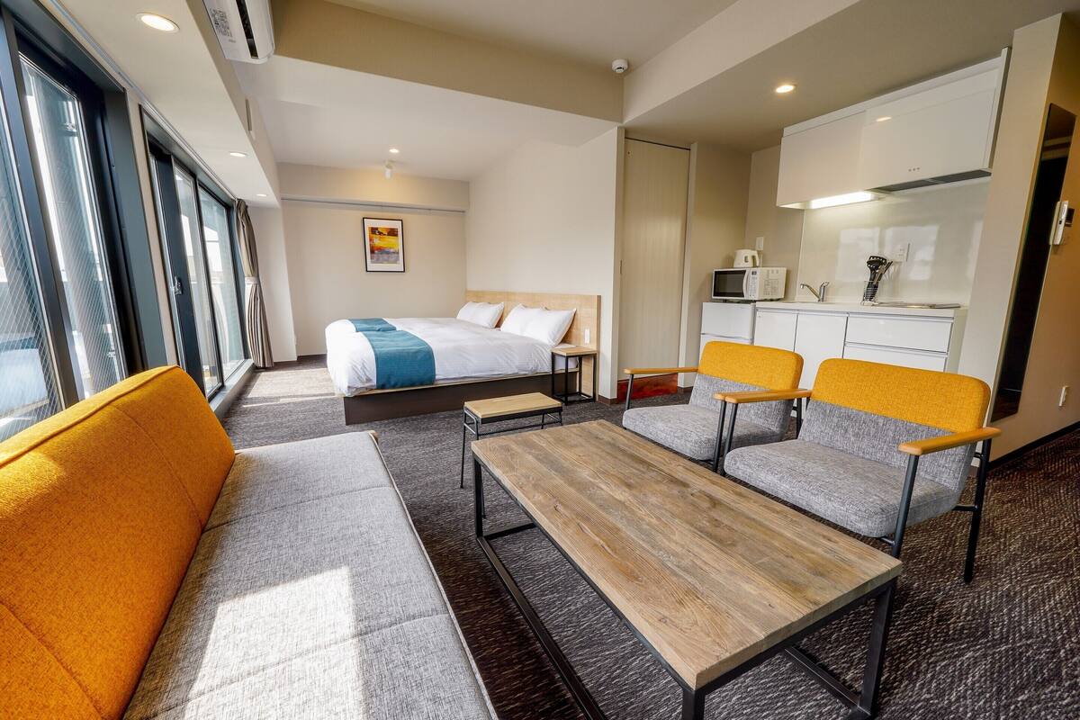 A modern hotel room with a bed, a sofa, a coffee table, and a kitchenette.