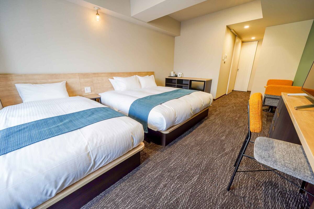 A hotel room with two beds, a desk, and a chair.