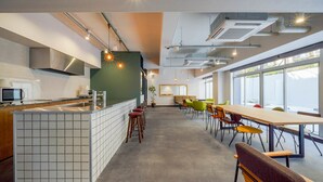 A modern kitchen with a tiled island, bar stools, and a long dining table with colorful chairs. - RESI STAY HEART (Kyoto)
