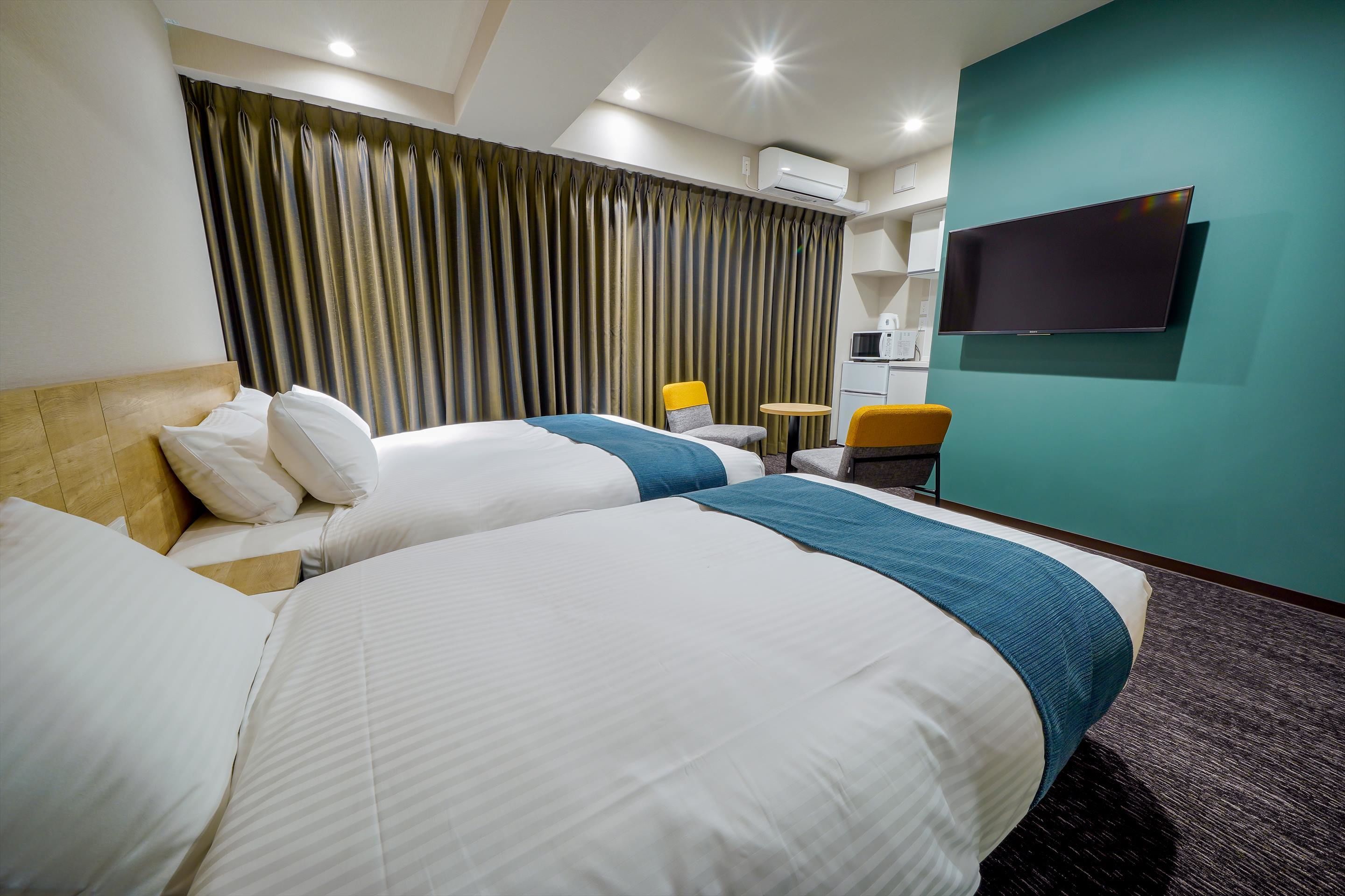 A hotel room with two beds, a TV, a small table, and a chair.