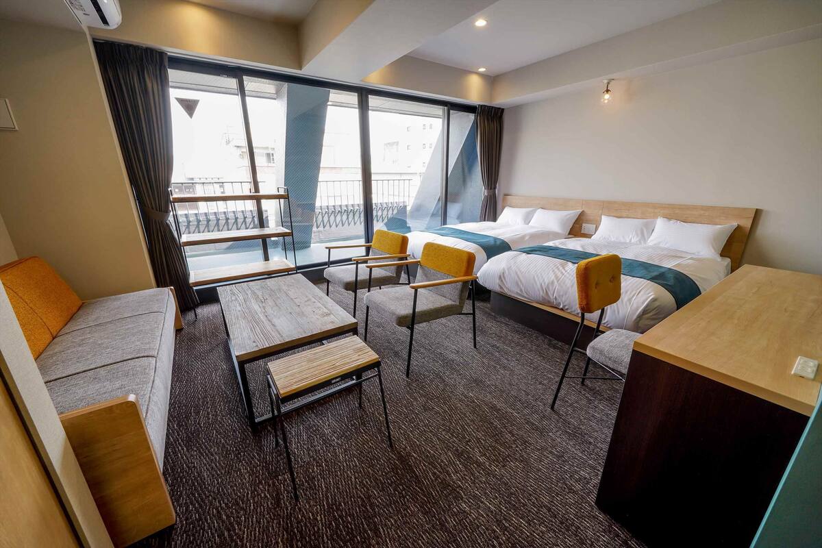 A hotel room with two beds, a sofa, a small table, and a chair.