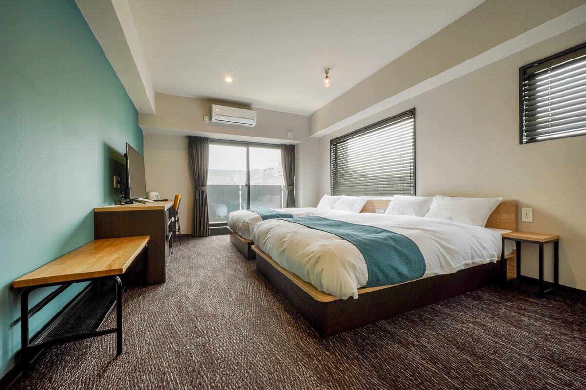 A hotel room with a bed, desk, and a view of the city through the window.