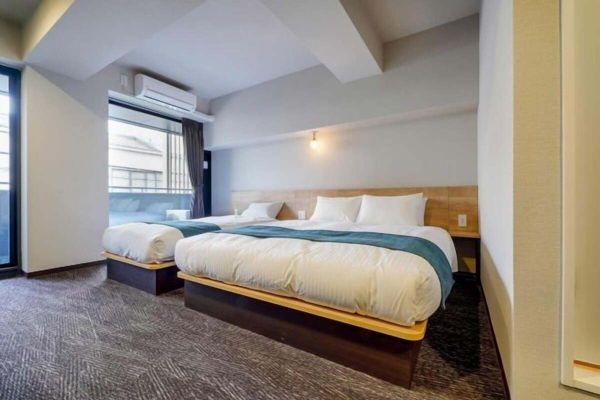 A hotel room with a large bed, a bedside table, a window with curtains, and an air conditioning unit.