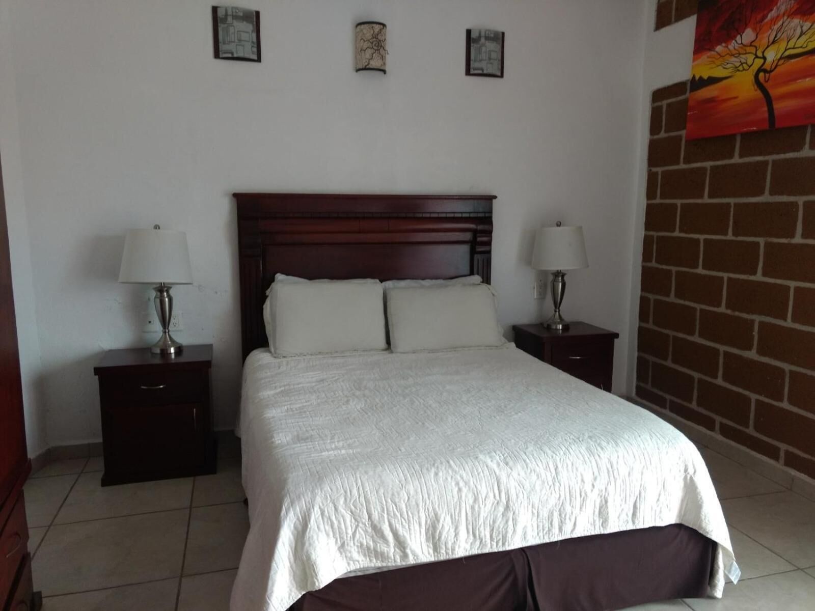 A bedroom with a large bed, two bedside tables with lamps, and a brick wall.