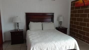 A bedroom with a large bed, two bedside tables with lamps, and a brick wall.