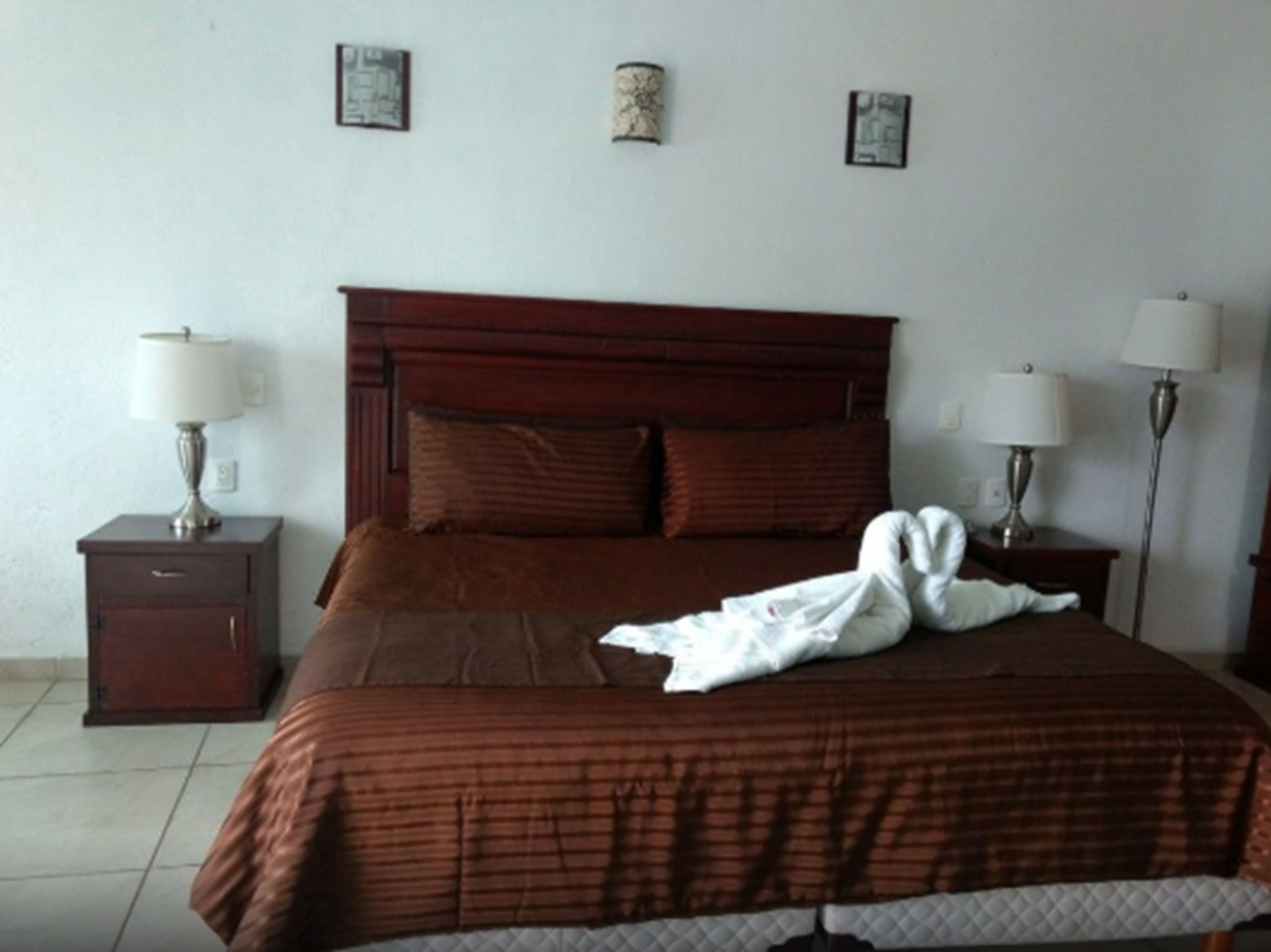 A hotel room with a large bed, two bedside tables with lamps, and three framed pictures on the wall.