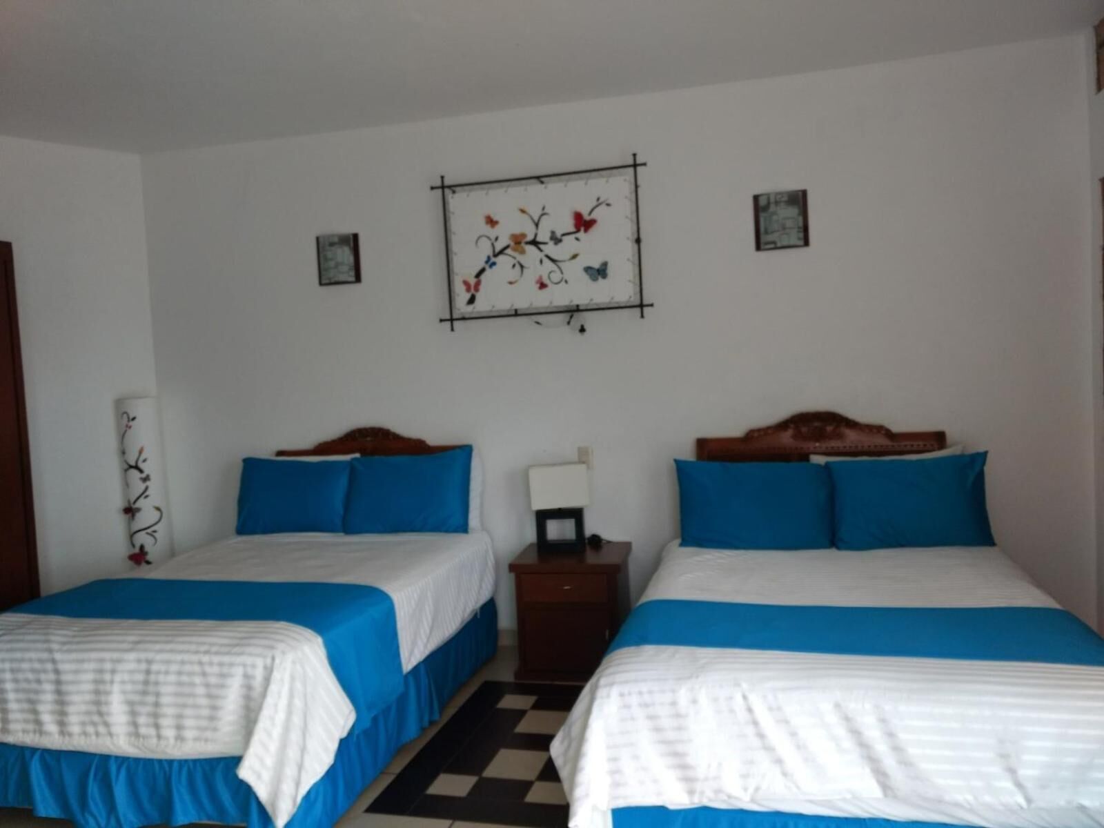 A room with two beds, each with blue and white bedding, a checkered floor, and a wall-mounted artwork.