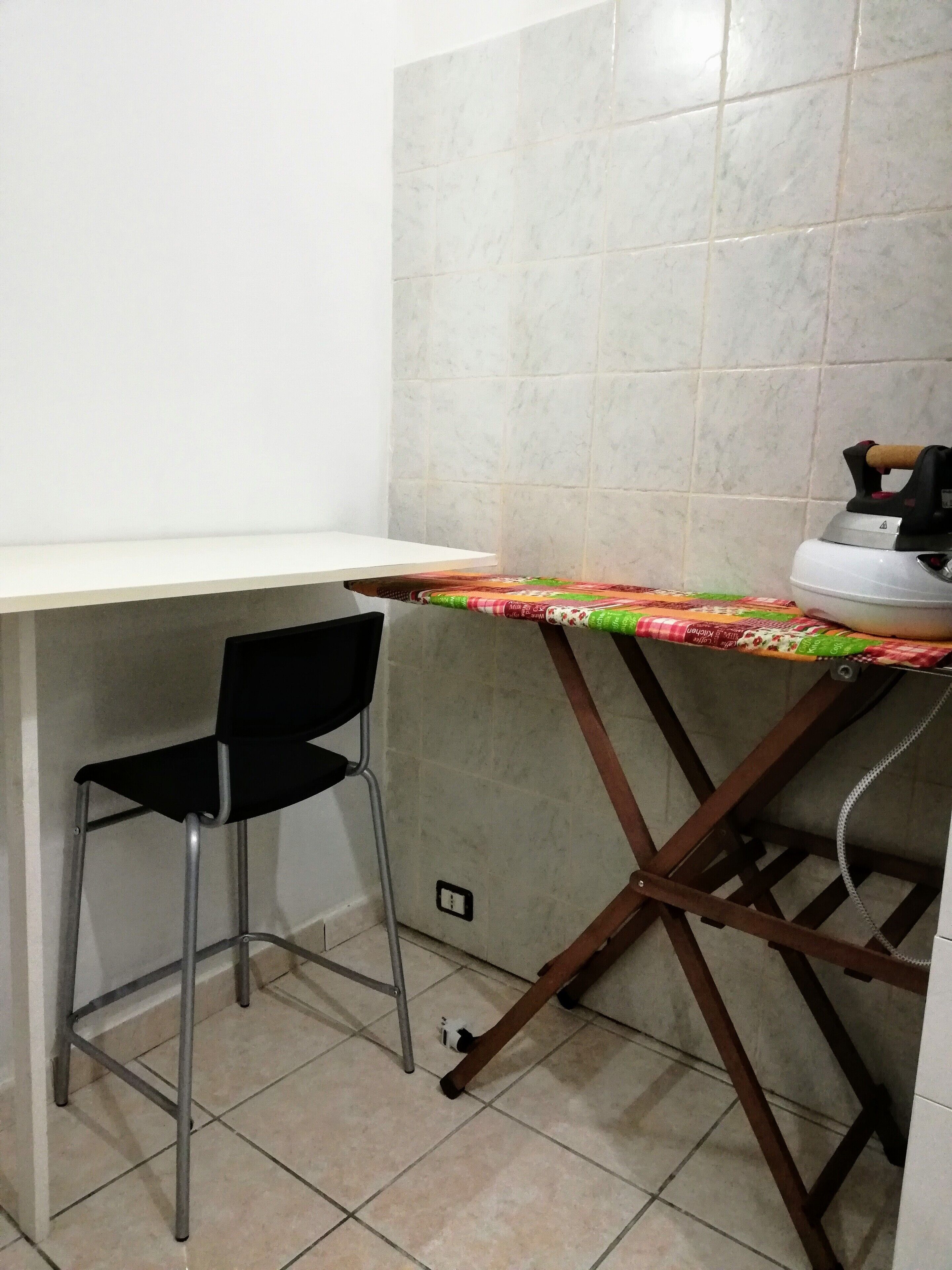 Una cocina con mostrador blanco, una silla negra y una mesa con mantel colorido.