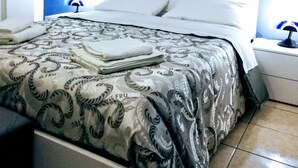 A neatly made bed with a patterned bedspread, white pillows, and folded towels on a white nightstand with a lamp. - Catania House single apartment sleeps 4 near the new Garibaldi  (Catania)