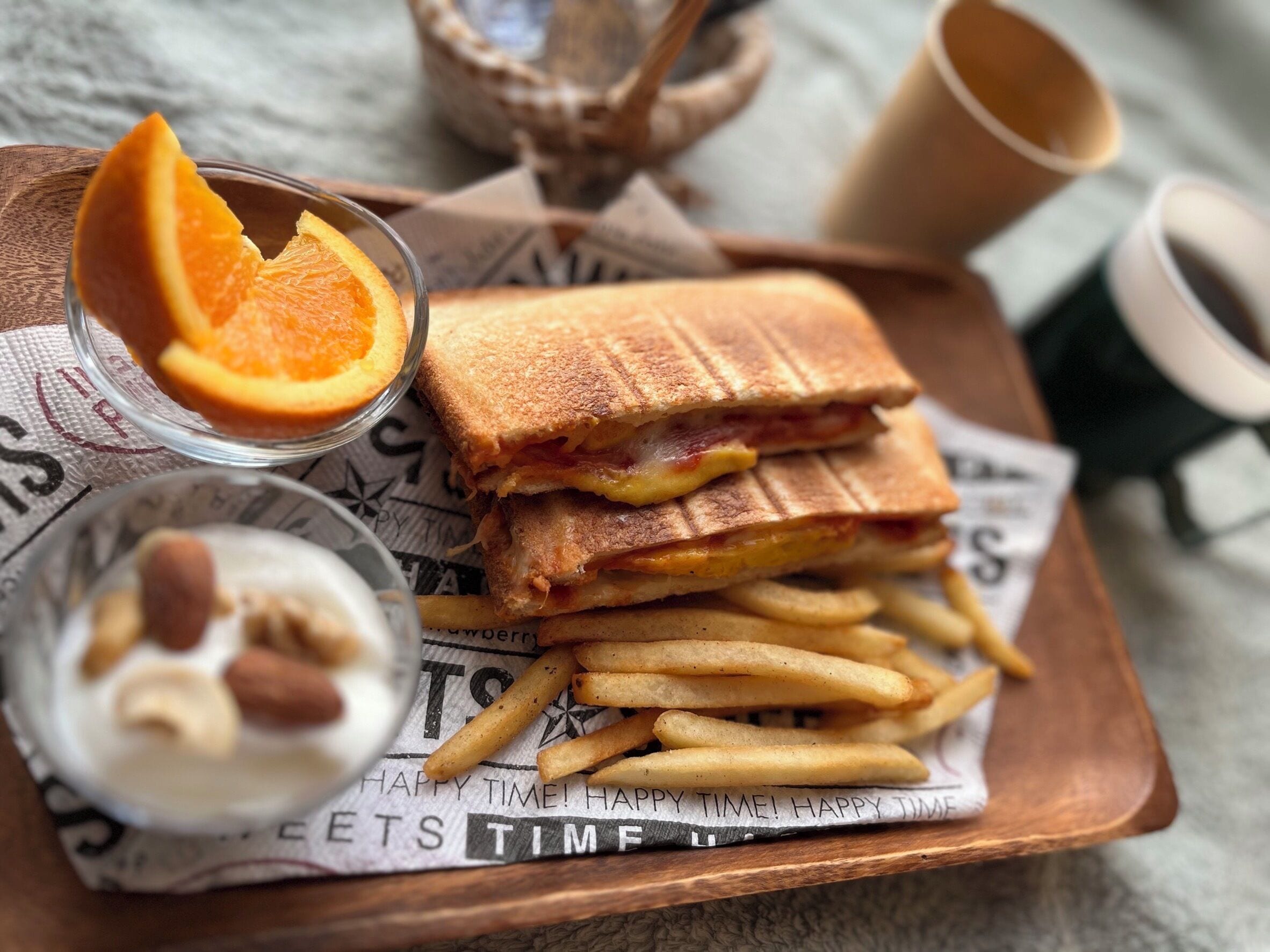 En bakke med en panini, pommes frites, en skål med nødder og et glas appelsinjuice.