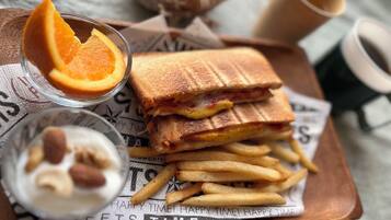 Una bandeja con un sándwich de queso a la plancha, papas fritas, un cuenco pequeño de nueces y un vaso de jugo de naranja.