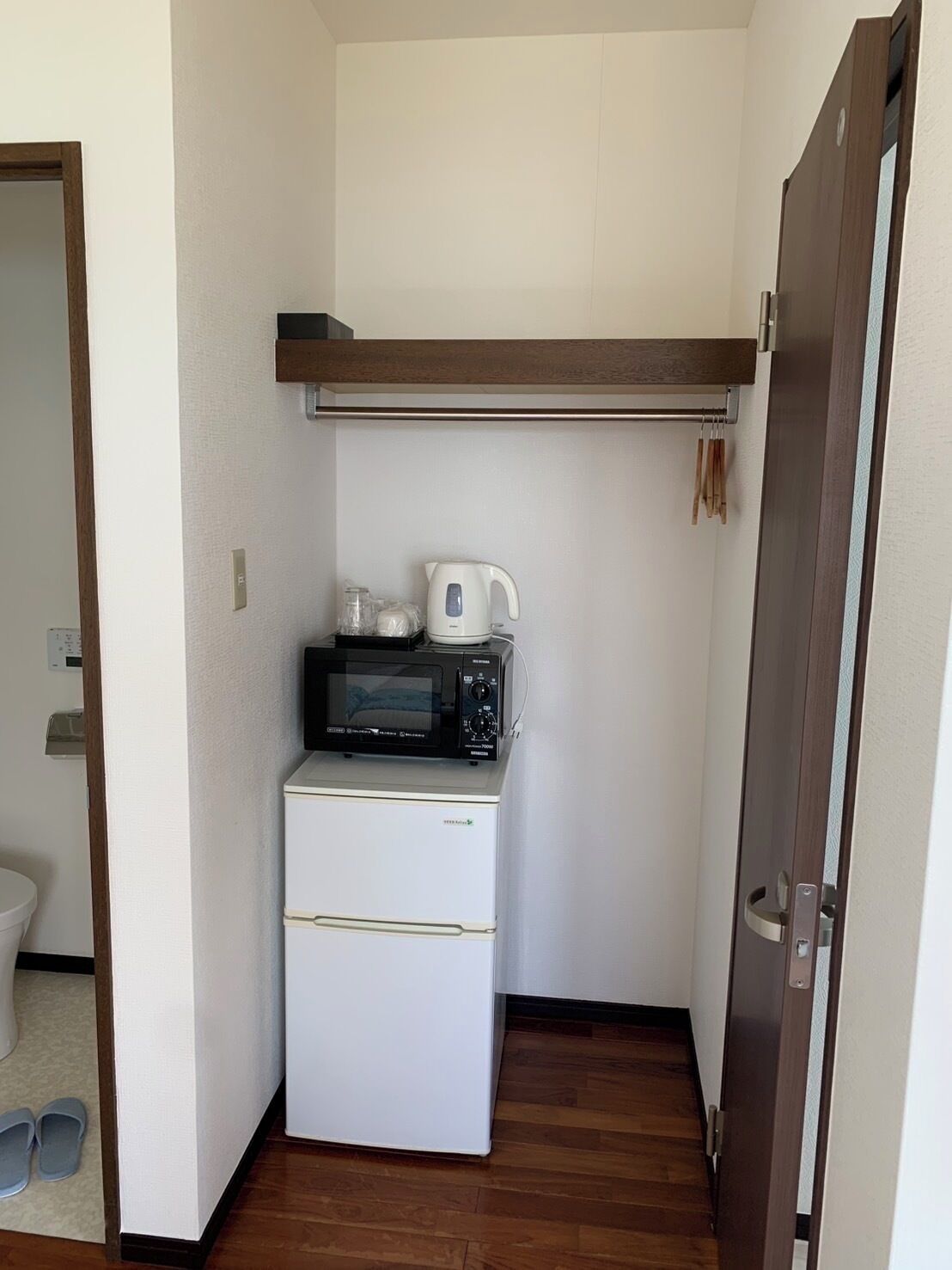 Cocina compacta con refrigerador, microondas, tetera y un estante pequeño.