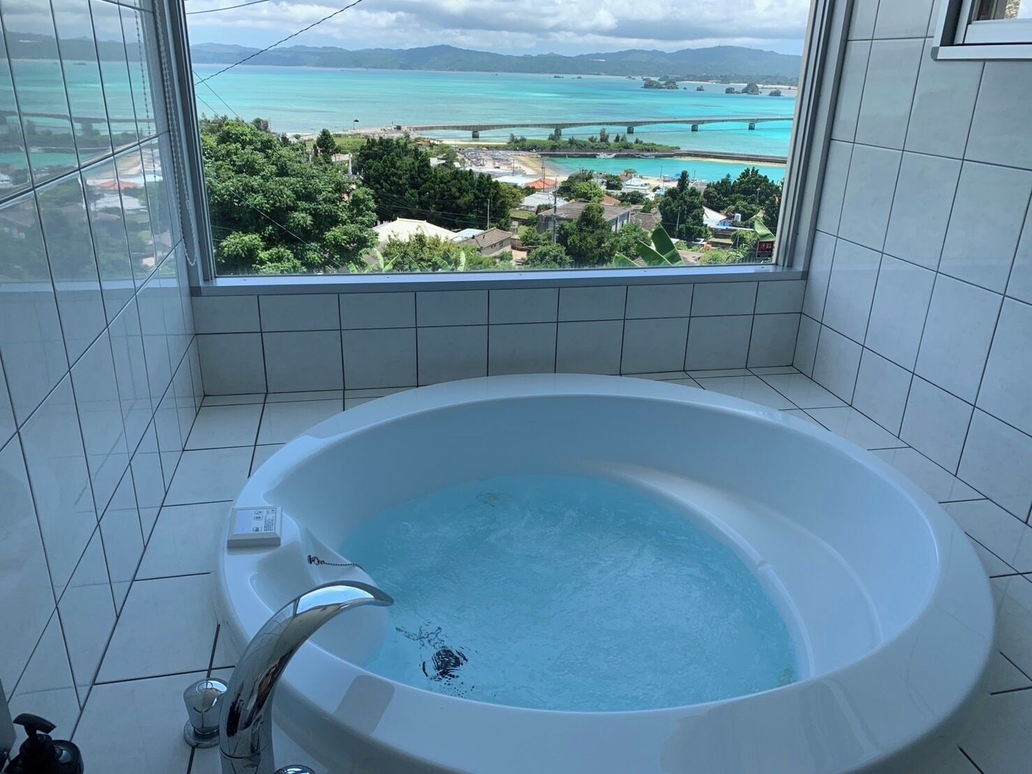 A bathroom with a large bathtub, a view of a coastal area, and tiled walls.