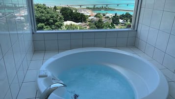 A bathroom with a large bathtub, a view of a coastal area, and tiled walls.