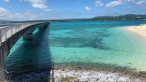 A coastal bridge over turquoise waters with a beach and distant hills. - Seabreeze Kouri (Nakijin)