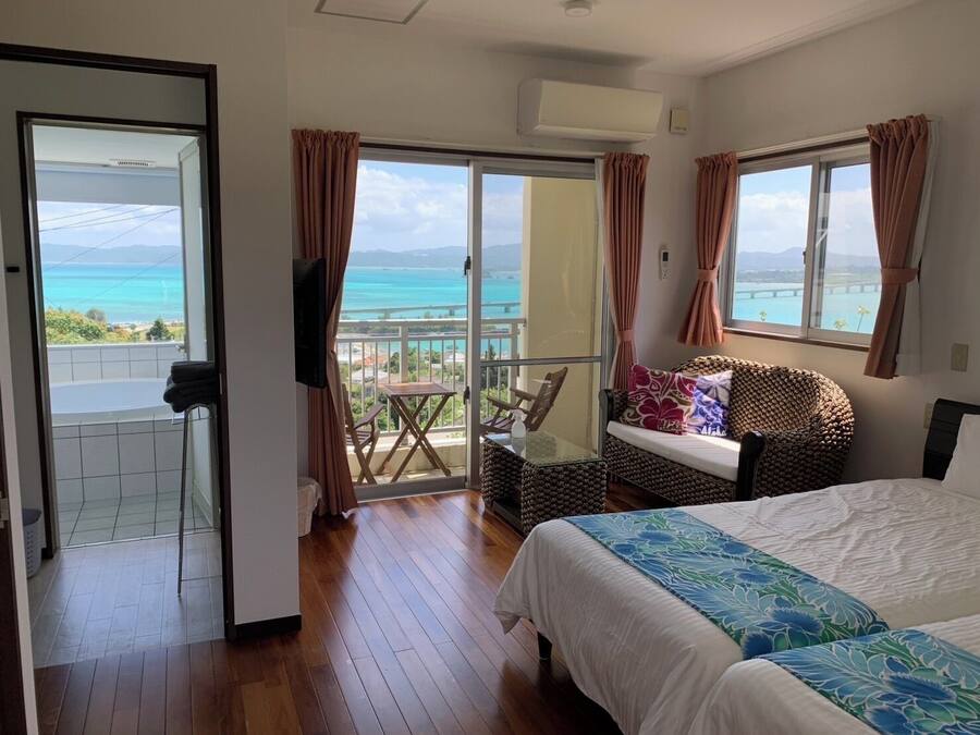 A bedroom with a balcony, a bed, a sofa, and a TV.