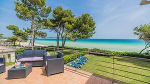 Un balcon agrémenté de meubles en osier, une vue sur la mer et un espace verdoyant avec des chaises longues bleues.