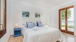 Une chambre à coucher avec un lit, des tables de chevet, des œuvres d’art et une vue sur l’extérieur, visible à travers une porte.