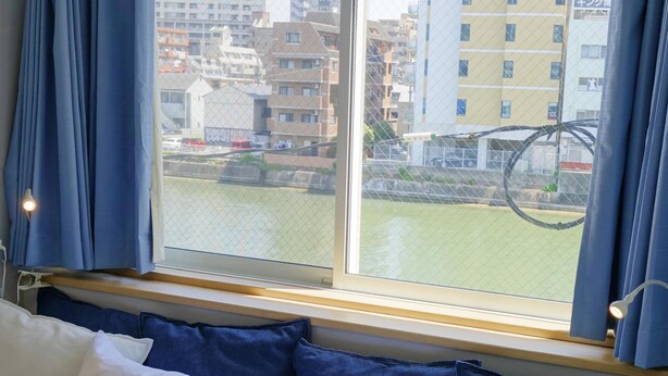 Une chambre d’hôtel avec un lit, une fenêtre avec des rideaux bleus et une vue sur des bâtiments et une étendue d’eau.