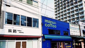 Un bâtiment bleu avec une enseigne indiquant « Manu Coffee » et une autre, sur le bâtiment blanc adjacent, indiquant « Tabiji Hostel ».