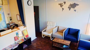 Une pièce chaleureuse avec un plancher en bois, un fauteuil blanc, un fauteuil bleu et une petite table en bois. Une carte du monde est accrochée au mur et une horloge se trouve au-dessus de la porte.