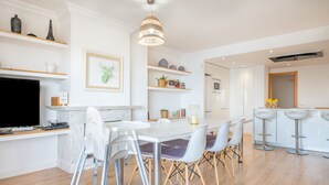 Una cocina moderna con armarios blancos, un comedor con sillas blancas y una barra con taburetes.