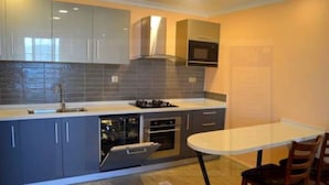 A modern kitchen with grey cabinets, a built-in oven, and a white dining table. - Serene Crest Apartments (Kigali)