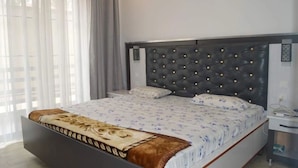 A bedroom with a large bed, a dark headboard with lights, a bedside table, and a window with curtains. - Serene Crest Apartments (Kigali)
