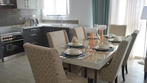 A modern dining area with a glass table, patterned chairs, and a kitchen in the background. - Serene Crest Apartments (Kigali)