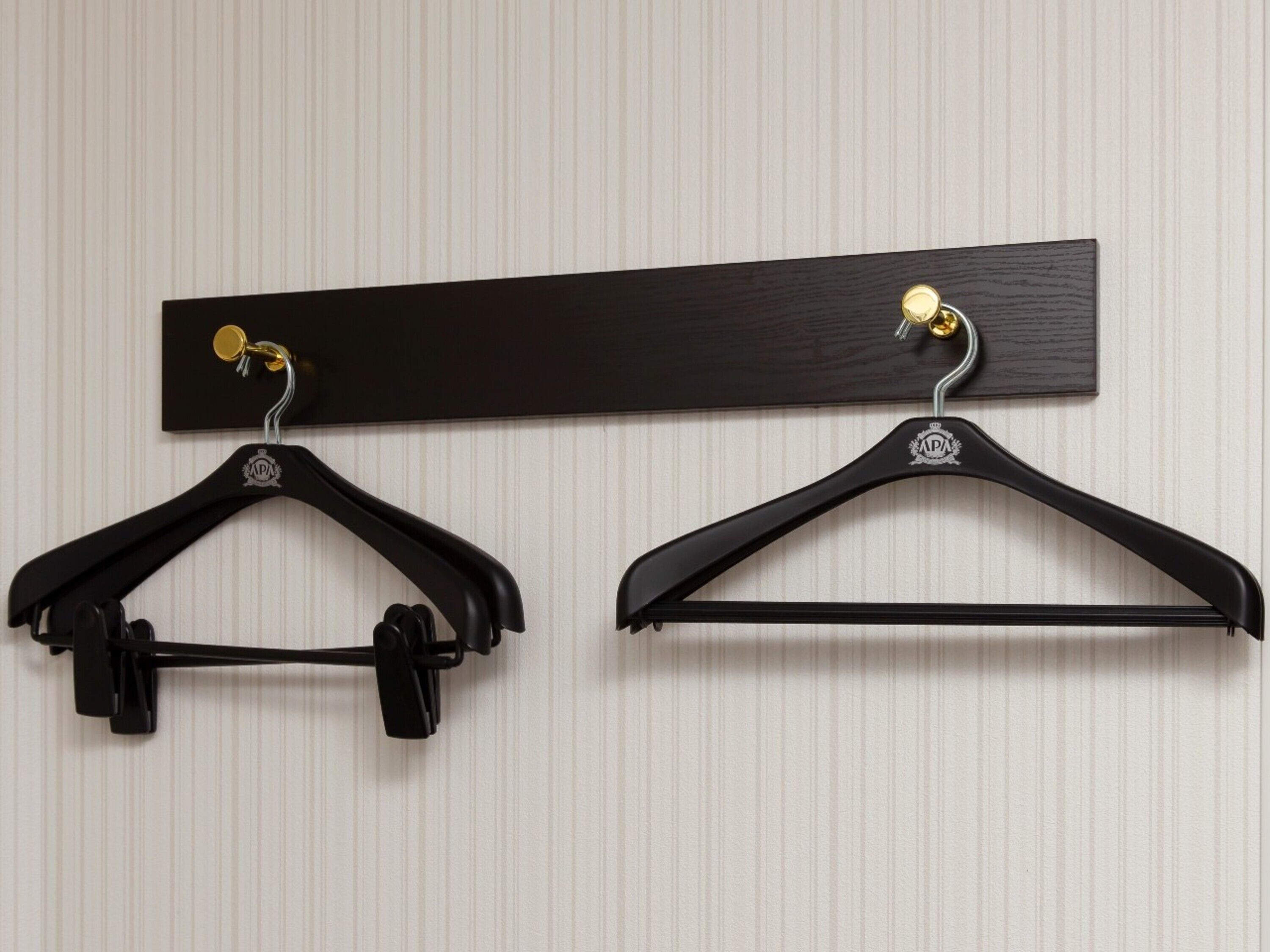 Two black hangers with gold hooks on a wooden board against a striped wall.