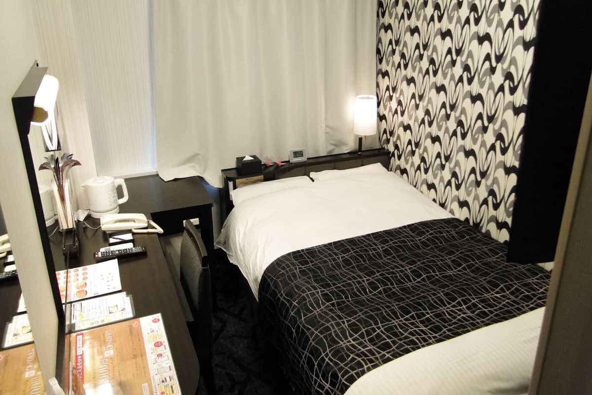 A hotel room with a bed, a desk with a telephone, a lamp, and a window with curtains.