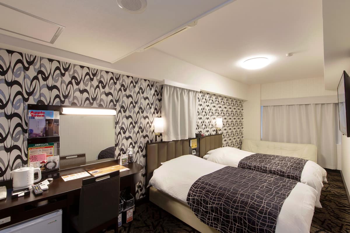 A hotel room with two beds, a desk with a coffee maker, a TV, and a patterned wallpaper.