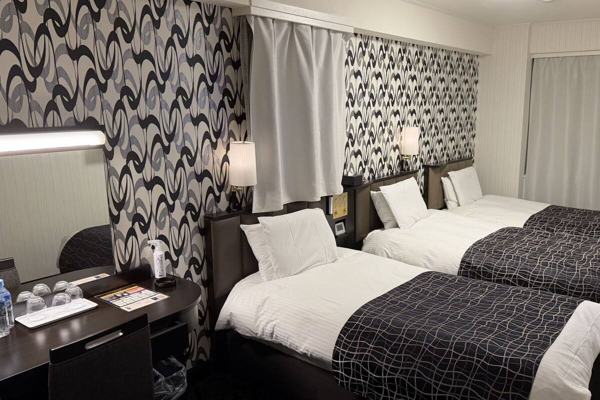 A hotel room with two beds, a desk with a computer, a chair, and a window with curtains.